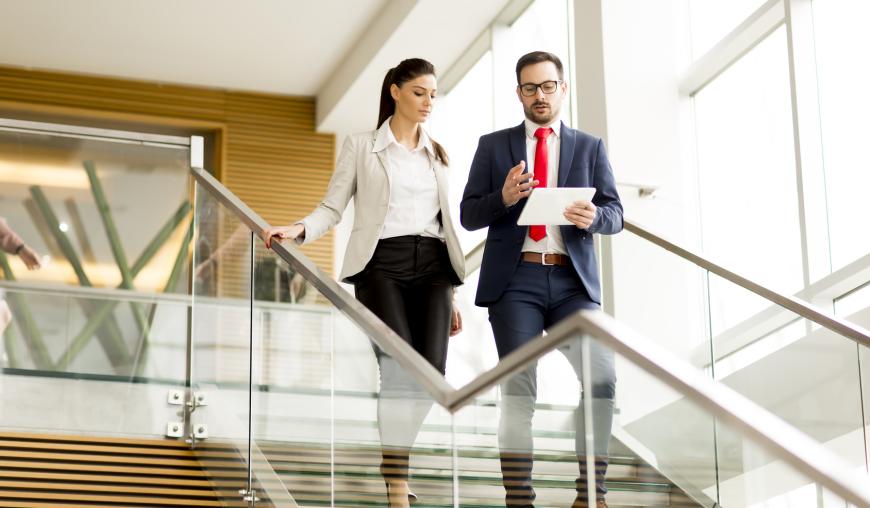 Eine Frau und ein Mann gehen gemeinsam eine verglaste Treppe hinunter und besprechen etwas.