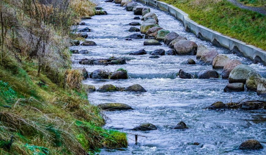 Flussbett mit kleinen und großen Steinen und leichter Strömung des Wassers (Fischtreppe Torgelow)