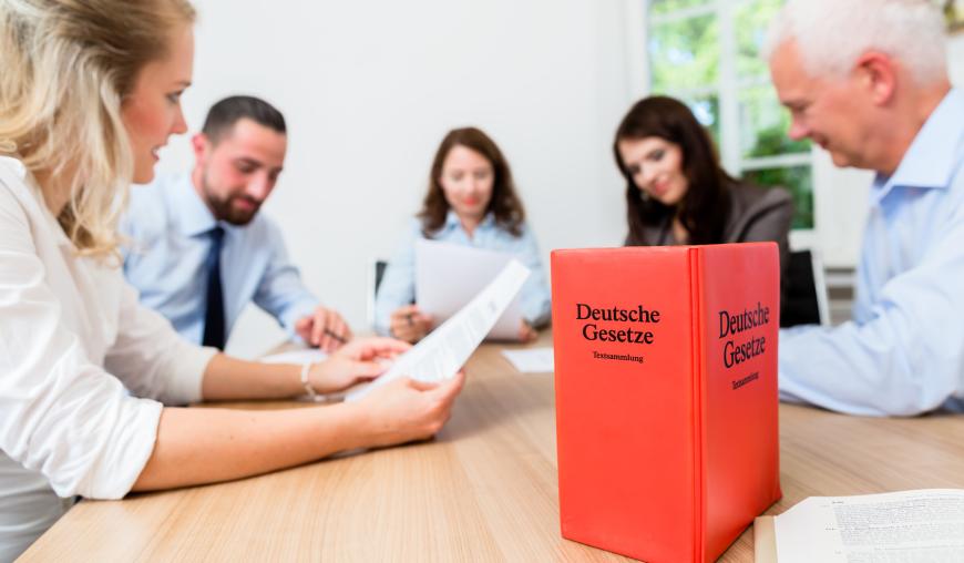 Drei Frauen und zwei Männer diskutieren konzentriert über ein Papier. Im Vordergrund steht die Gesetzessammlung "Deutsche Gesetze".