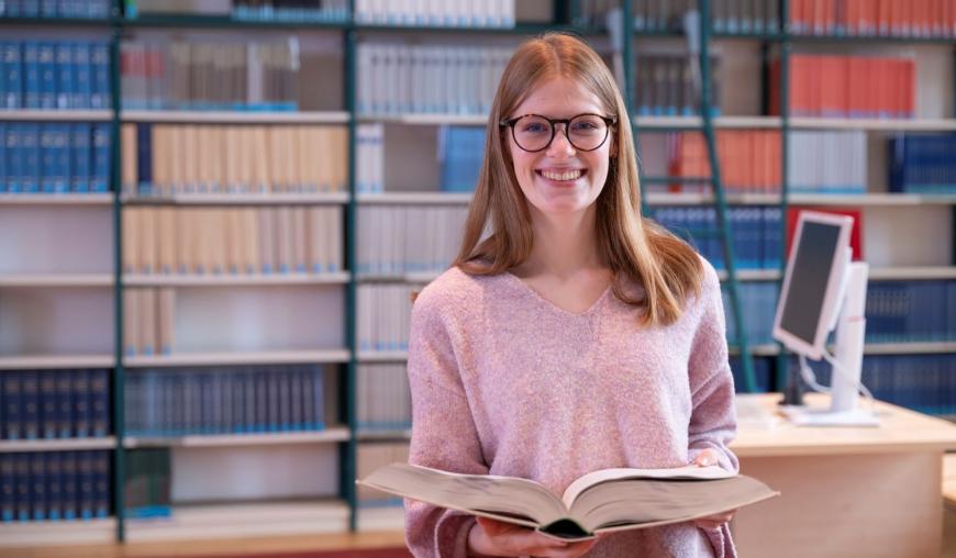Frau hält ein Gesetzestext vor einem Bücherregal